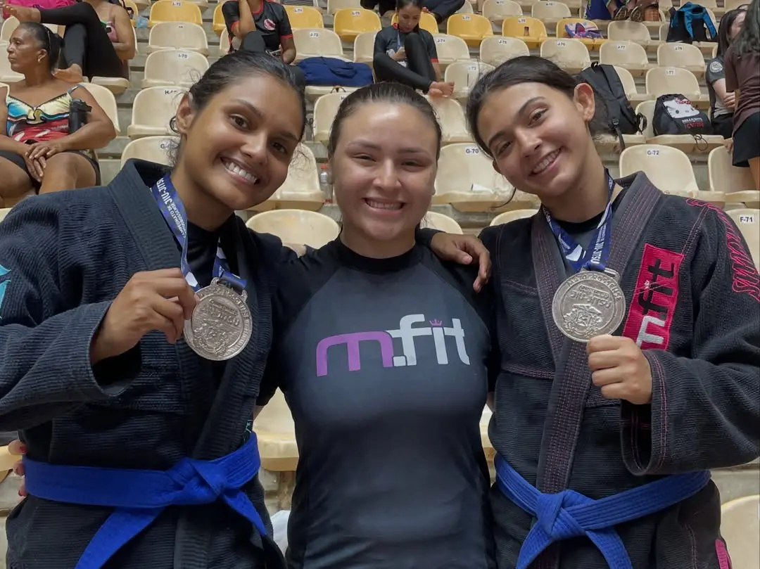 Três alunas da MFIT sorrindo com medalhas de prata depois de um campeonato de jiu-jitsu