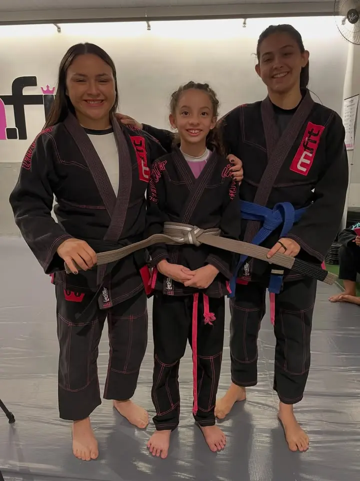 Menina graduada de faixa cinza entre duas alunas adultas